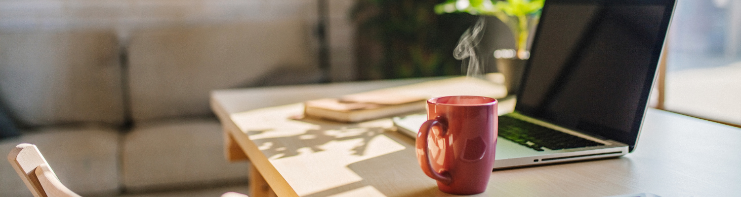 Sun-lit tabletop with a laptop, notebook, and coffee mug